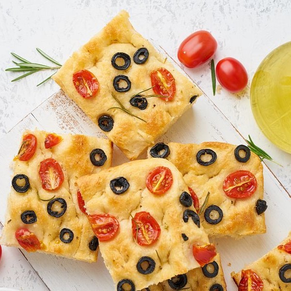 Sliced pieces of a focaccia with tomatoes, olives and rosemary. Copy space for text. Traditional Italian flat bread. Top view.