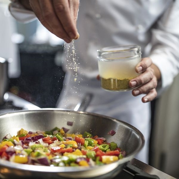 Chef seasoning pan of vegetables on stove, close-up