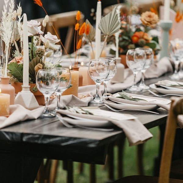 Event and catering agency organization modern wedding in boho style. Table for guests assembled with dishes, cutlery, glasses and flowers, candles and elements, chairs on green lawn, flat lay, outdoor