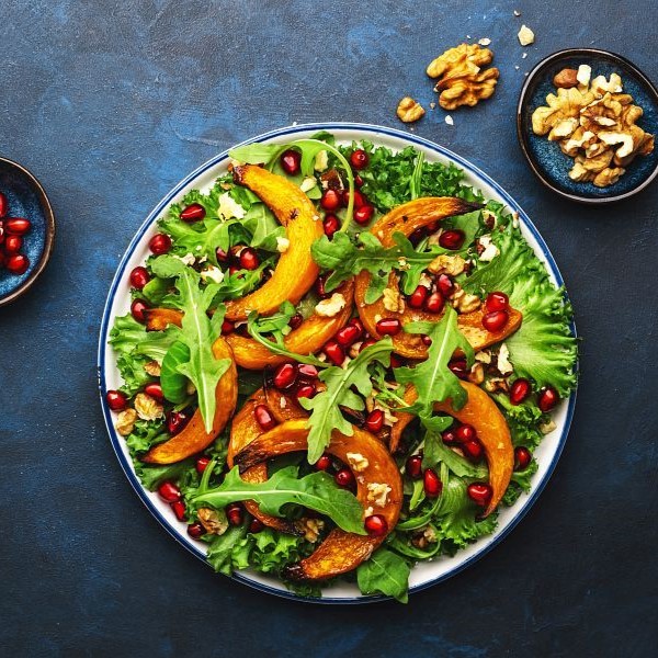 Healthy vegan eating, autumn pumpkin salad with baked honey pumpkin slices, lettuce, arugula, pomegranate seeds and walnuts. Comfort food. Top view